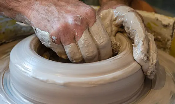 Hands molding clay on a pottery wheel