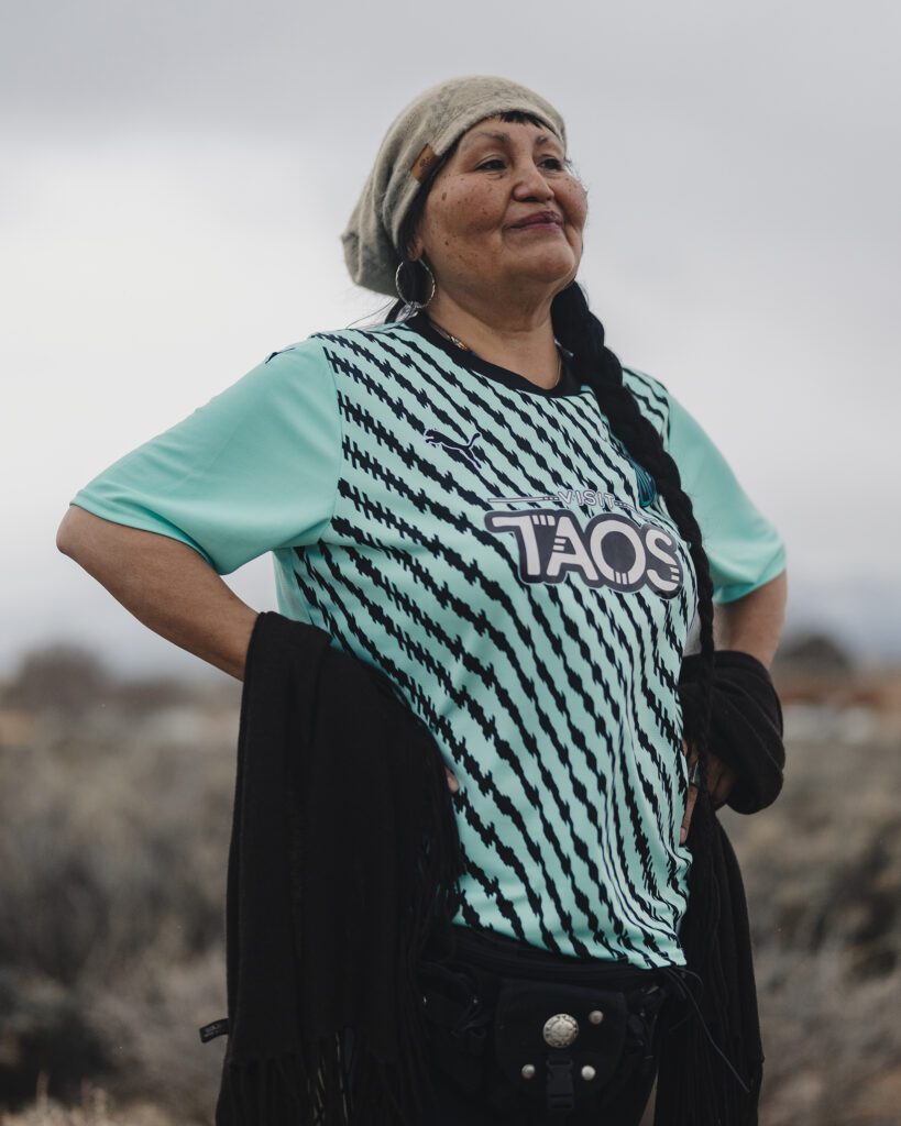 A woman wearing a striped turquoise jersey that says Visit Taos