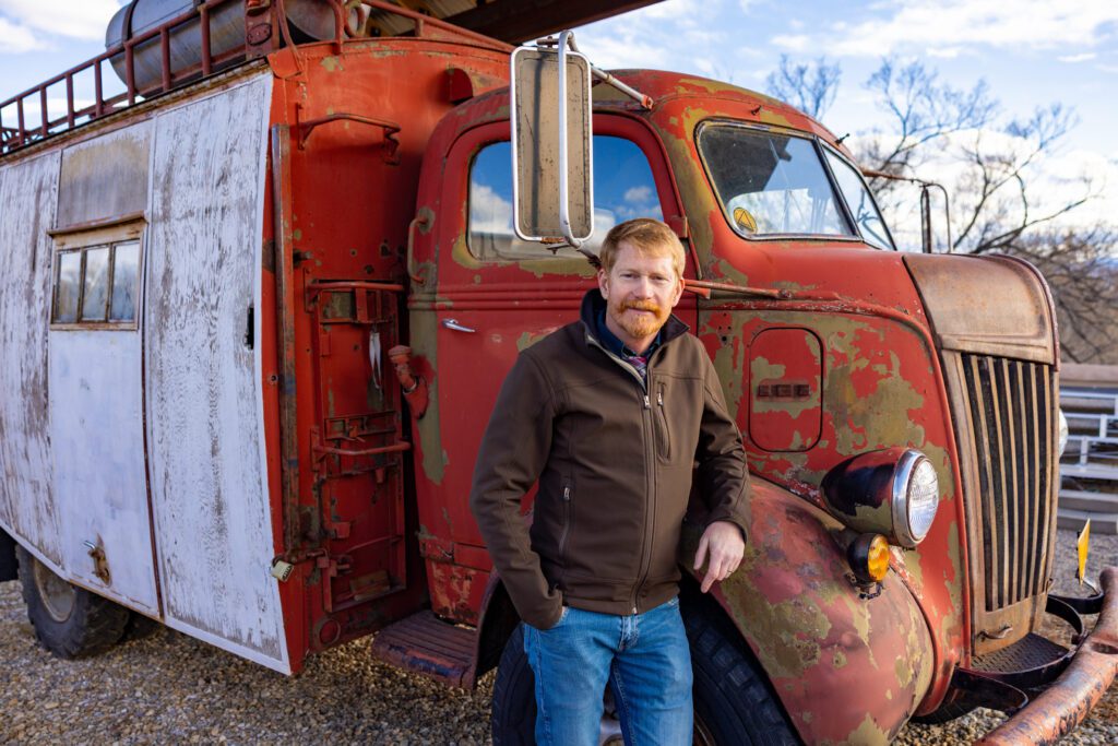 A man leans against a red antique truck.