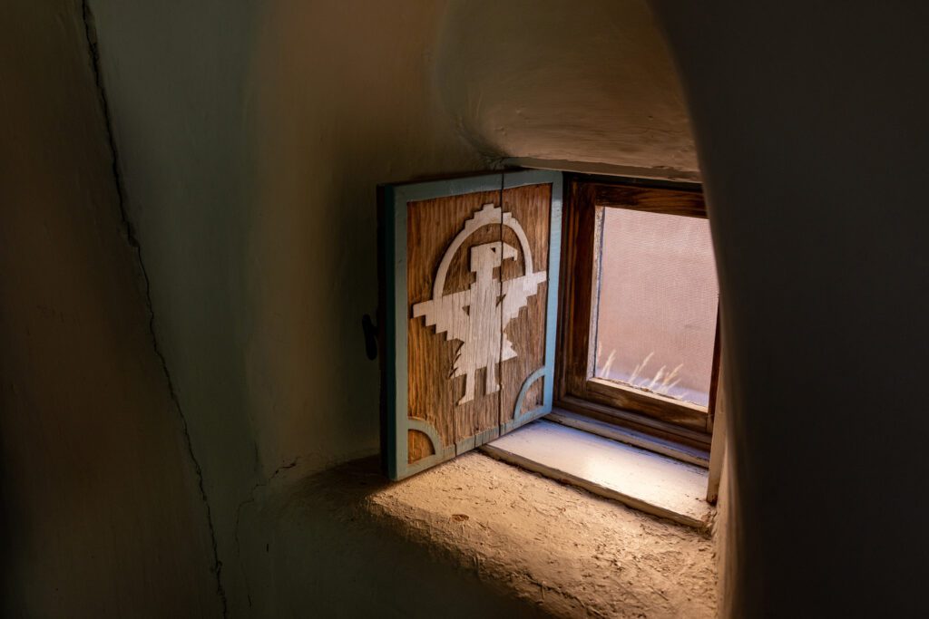 A small window with a hand-caved shutter of featuring a bird