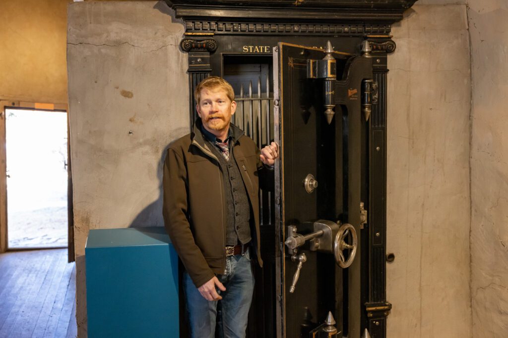 A man stands in front of large, old-style safe