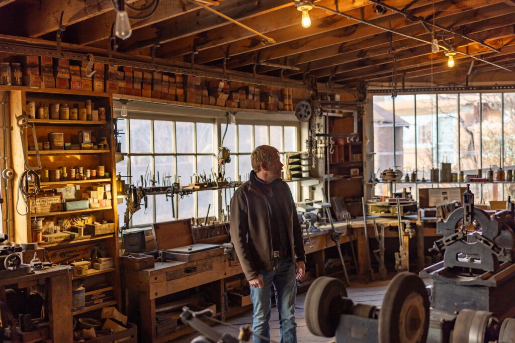 A man in a workshop with various antique tools.